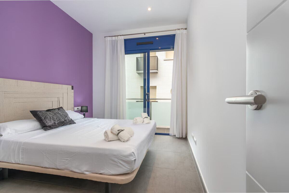 Habitación de hotel con cama, ventana con cortinas, puerta y vista a un edificio.