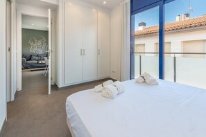Ein Schlafzimmer mit Bett, Kleiderschrank und Blick auf ein Gebäude durch ein Fenster.