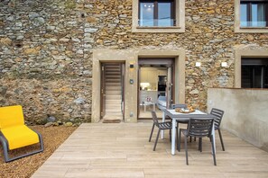 Ein Steinhaus mit einer Terrassenfläche, komplett mit Tisch und Stühlen, einem gelben Sessel und einer Treppe zu einem Innenbereich.