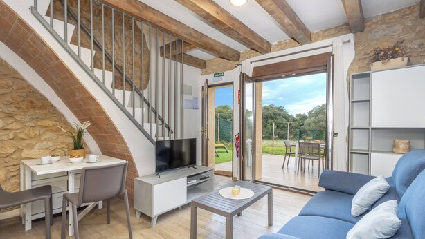 Una sala de estar moderna con televisor, asientos, una escalera y vistas al exterior.