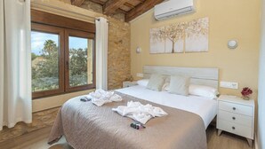 Un dormitorio con una cama grande, paredes de piedra, techo de madera, aire acondicionado, una mesita de noche y una ventana con cortinas.