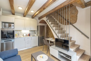 A modern kitchen with built-in appliances, a dining area, a TV on a white console, and a staircase with a stone accent.