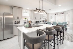 Une cuisine moderne dotée d’un grand îlot central, de tabourets de bar et d’appareils électroménagers en acier inoxydable.
