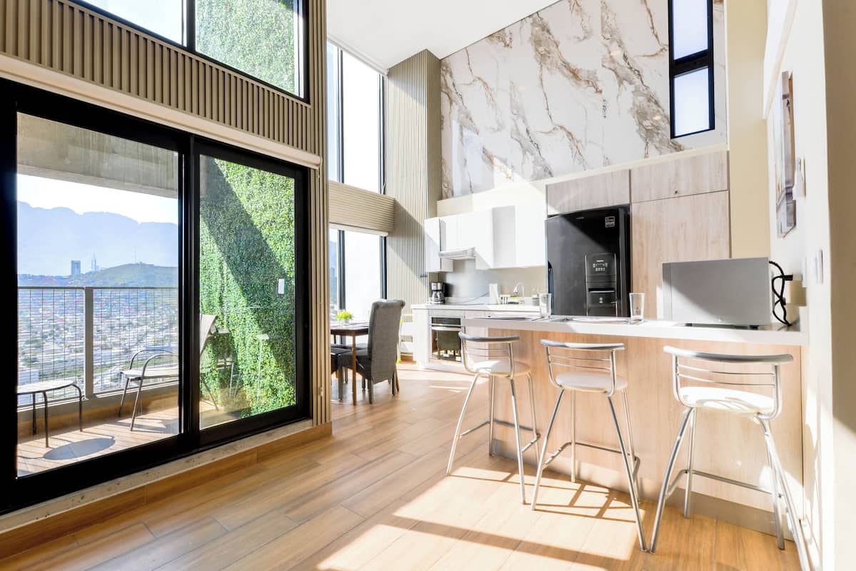 A modern kitchen with a large island, bar stools, and a view of a cityscape through large windows.