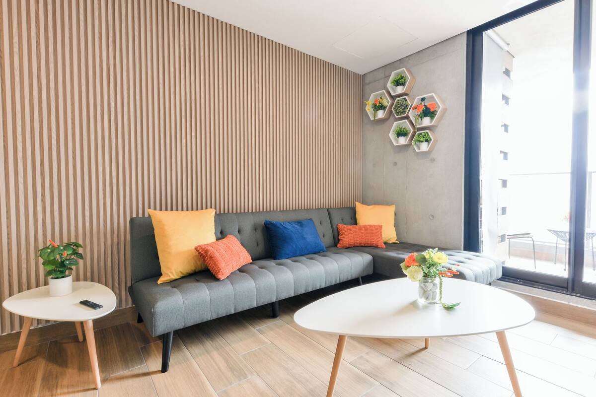 A modern living room with a grey sofa, two round tables, and a large window.