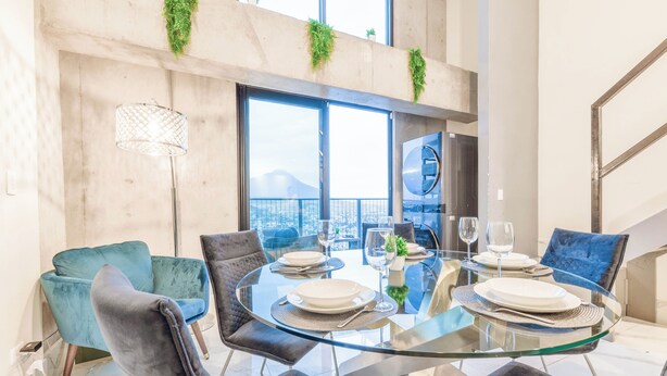 Un espace repas moderne avec une table en verre, des fauteuils en velours et une vue sur la ville.