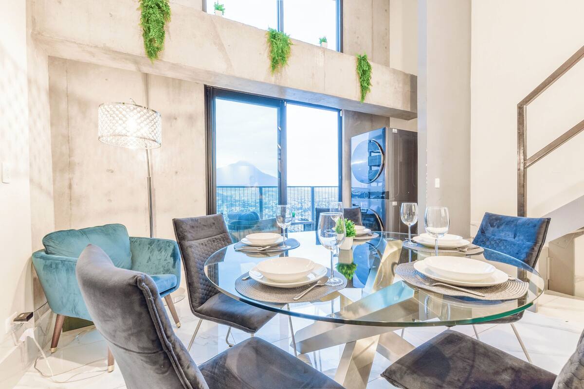 A modern dining area with a glass table, velvet chairs, and a view of the city.