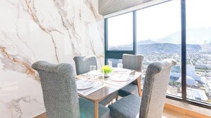 Un coin repas agrémenté d’un mur en marbre, d’une grande fenêtre offrant une vue sur la ville et d’une table dressée pour quatre personnes.