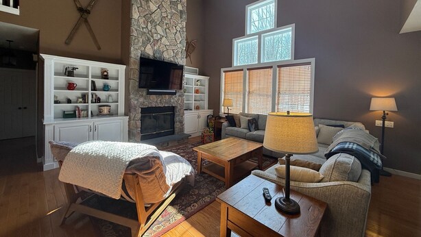 A living room with a stone fireplace, a television, a sofa, a coffee table, and a lamp. - Tremendous 5-bedroom house in Pocono Pines (Pocono Pines)