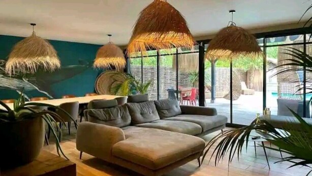 A modern living room with a sectional sofa, hanging rattan lamps, and large windows offering a view of the outdoors. - Villa Patio Bleu, heated pool, center & beach (Arès)