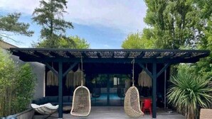 A pool area with a pergola, two hanging chairs, and a lounge chair. - Villa Patio Bleu, heated pool, center & beach (Arès)