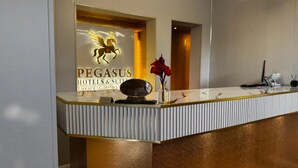 Un comptoir d’accueil aux couleurs or et blanc, un logo représentant un cheval et l’inscription « PEGASUS HOTELS & SURREY », ainsi qu’un vase rouge contenant une fleur.