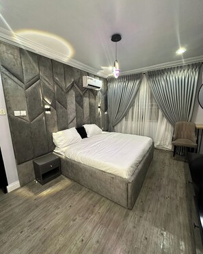 A modern bedroom with a large bed, a nightstand, a chair, and a desk. - Pegasus Hotel And Suites (Abuja)