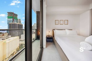 A hotel room with a large bed, a nightstand, and a view of the cityscape through a large window. - High-Rise Miami Condo | Rooftop Pool | Sea View (Miami)