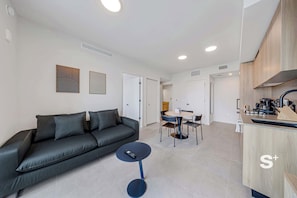 A modern living room with a dark grey sofa, a small round table, and a kitchen area with wooden cabinets and a sink. - High-Rise Miami Condo | Rooftop Pool | Sea View (Miami)