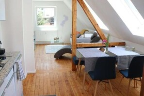 Ein Loft-Zimmer mit schrägem Dach, einem Esstisch mit Stühlen, einer Couch und Blick ins Freie.