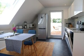 Eine kleine Küche mit Kühlschrank, Mikrowelle und Herd. Ein Esstisch mit Stühlen und ein Fenster sorgen für natürliches Licht.