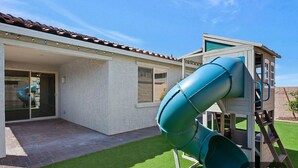 Una proprietà residenziale con patio coperto, area giochi con scivolo e una piccola casetta.