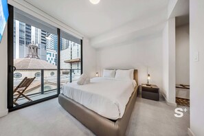 A modern hotel room with a large bed, a nightstand, and a view of a cityscape through floor-to-ceiling windows. - Rooftop Pool Oasis in Downtown Miami Condo w/ Gym (Miami)