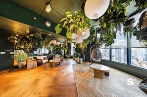 Een modern interieur met houten vloeren, zachte zithoek, hangplanten en grote ramen met uitzicht op de stad.