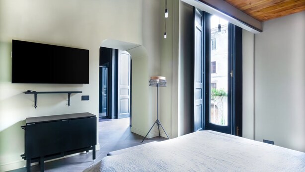 Een moderne slaapkamer met een groot bed, een wandgemonteerde televisie, een nachtkastje en een vloerlamp.