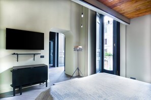 Ein modernes Schlafzimmer mit einem großen Bett, einem Wand-Fernseher, einem Nachttisch und einer Stehlampe.