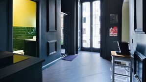 Een moderne hotel lobby met een receptiebalie, een zithoek met een wand betegeld in groen en geel, en een groot raam met uitzicht op de stad.