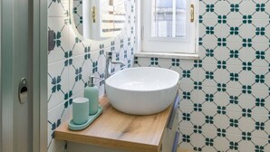 Een badkamer met een witte wastafel, een spiegel en een raam.