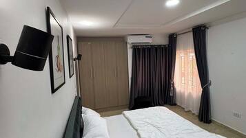 A bedroom with a bed, a wardrobe, an air conditioning unit, and a window with curtains.