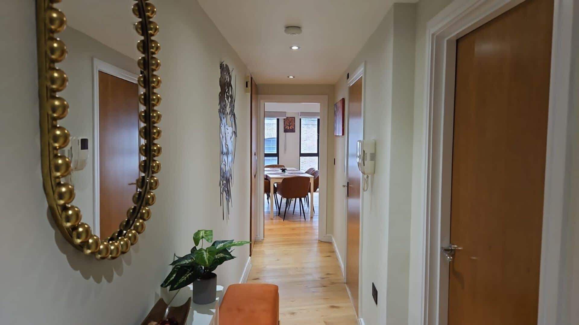 A hallway with a mirror, a potted plant, and a dining area in the distance.