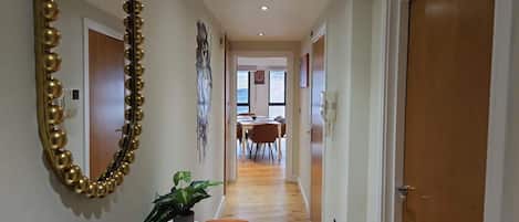 A hallway with a mirror, a potted plant, and a dining area in the distance.