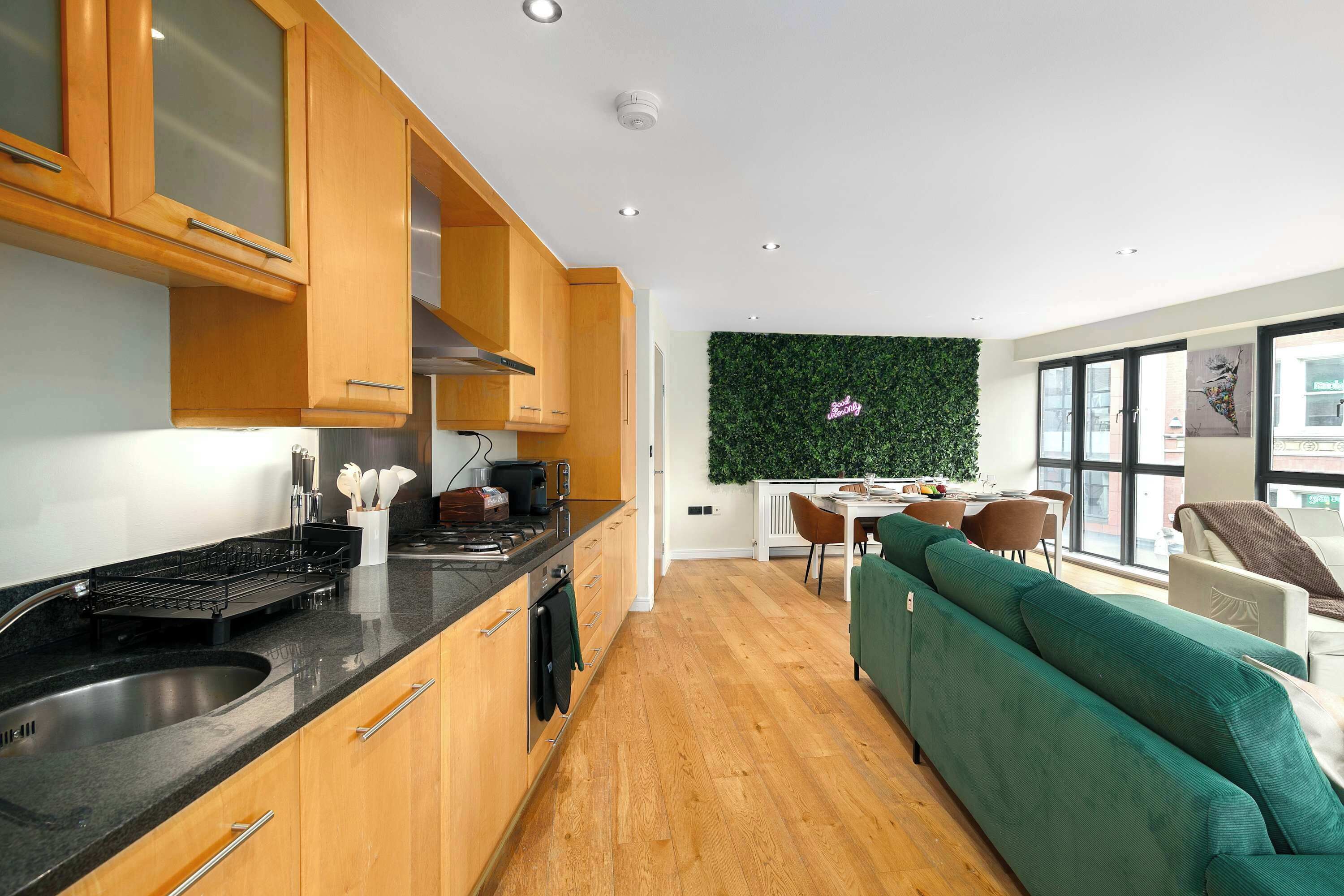 A modern kitchen with wooden cabinets, a black countertop, and a dining area with a green sofa and a white table.