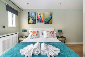 Een hotelkamer met een bed, twee nachtkastjes, een raam en drie vogelvluchtige schilderijen aan de muur.