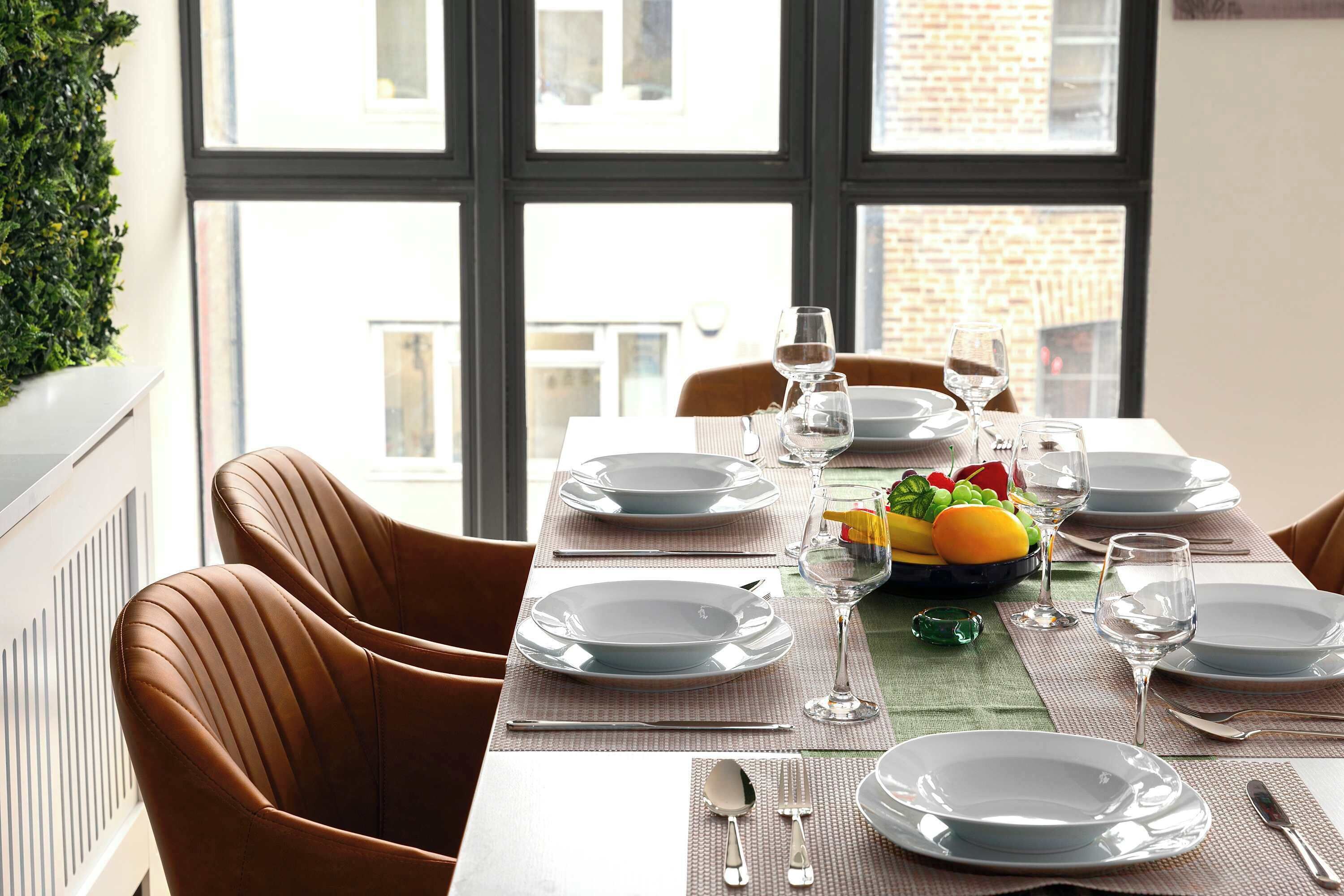 A dining table set with plates, glasses, and cutlery, with a fruit bowl on the table.