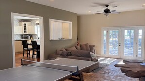 Una sala de estar con mesa de ping pong, sofá, mesa de comedor y cocina al fondo.