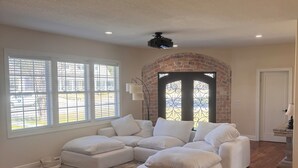 Un salón comedor amplio con sofá modular, ventanas grandes, chimenea y piso de madera.