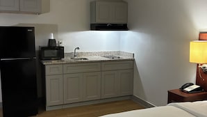A compact hotel room with a kitchenette, a bed, and a bedside table with a lamp. - Orange Studios (Orange)