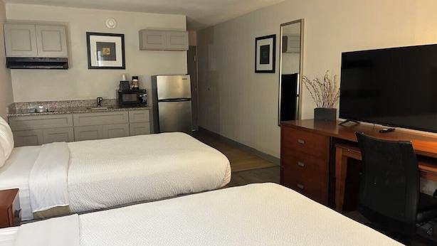 A hotel room with two beds, a desk with a TV, a microwave, and a refrigerator. - Orange Studios (Orange)