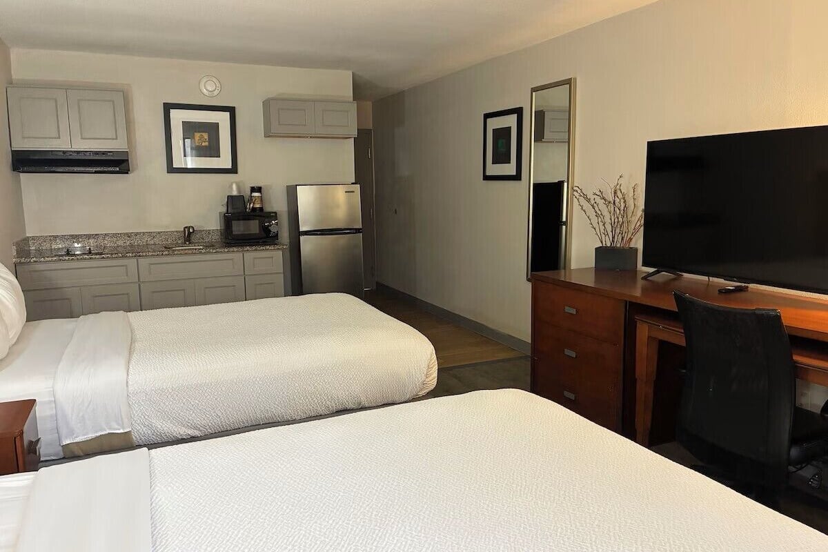 A hotel room with two beds, a desk with a TV, a microwave, and a refrigerator.