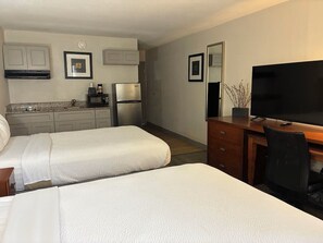 Une chambre d’hôtel avec deux lits, un bureau avec une télévision, un four à micro-ondes et un réfrigérateur.