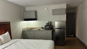A hotel room with a bed, a kitchenette with a microwave, a refrigerator, and a door leading to another room. - Orange Studios (Orange)