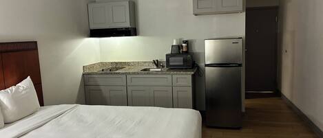 Una habitación de hotel con una cama, una kitchenette equipada con microondas, un refrigerador y una puerta que da a otra habitación.