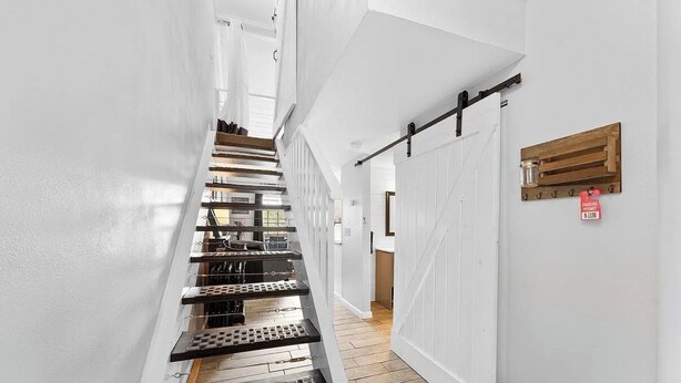 Una moderna scala con ringhiere in metallo e pavimento in legno, che conduce a una stanza con una porta a soffietto e una mensola con un barattolo.