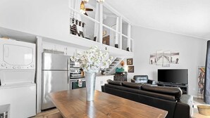 Una cucina moderna con elettrodomestici bianchi, un tavolo da pranzo con un vaso di fiori, un divano in pelle nera e una televisione a schermo piatto.