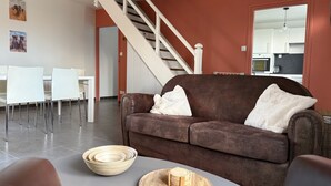 A living room with a brown sofa, white chairs, a dining table, and a staircase.