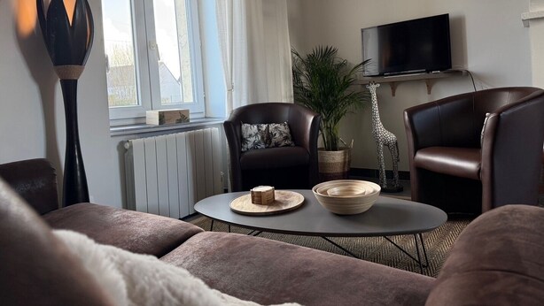 A living room with a sofa, two armchairs, a coffee table, a TV, and decorative items.