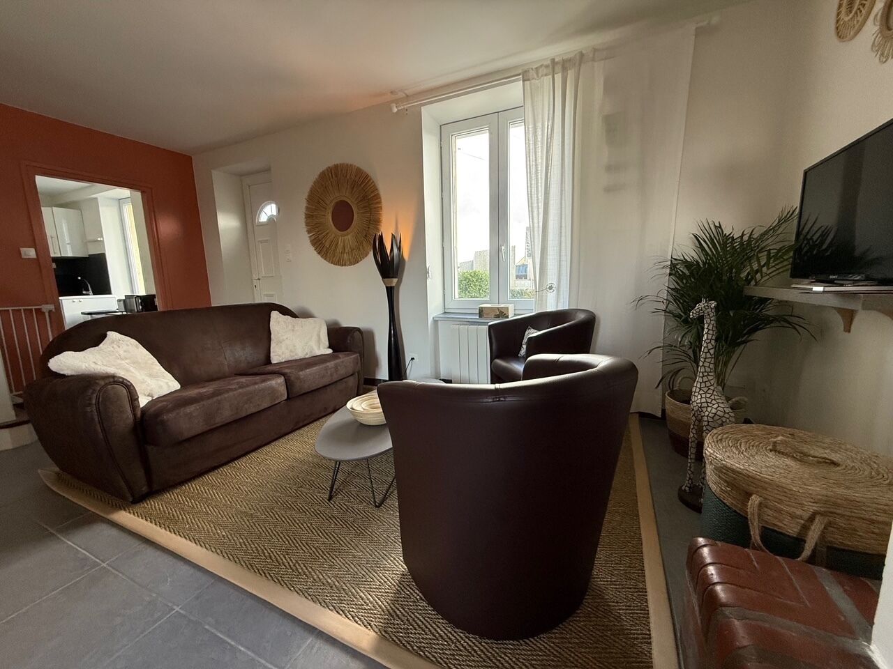 A living room with a brown sofa, a coffee table, a large armchair, a TV, and a giraffe statue.