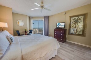 Une chambre d’hôtel comprenant un lit, un bureau avec une chaise, une télévision, un ventilateur de plafond et un balcon avec vue.
