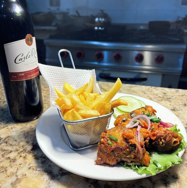 A plate with fried chicken, fries, and a bottle of wine on a kitchen counter. - The Bless Navic Hotel (Aba)