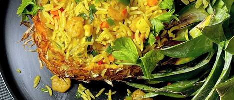 A plate of food with rice, vegetables, and a whole fish on a dark plate.